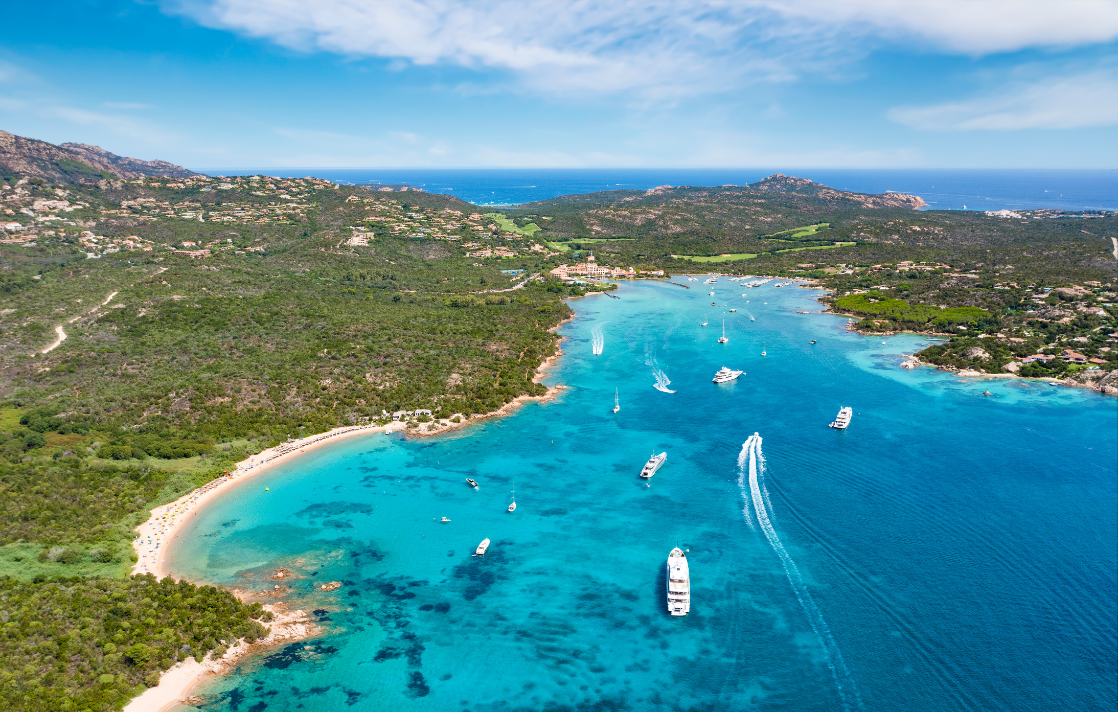 View from above, stunning aerial view of the Cala di volpe bay with a green coastline, white sand beaches and luxury yachts sailing on a turquoise water. Liscia Ruja, Costa Smeralda, Sardinia, Italy.